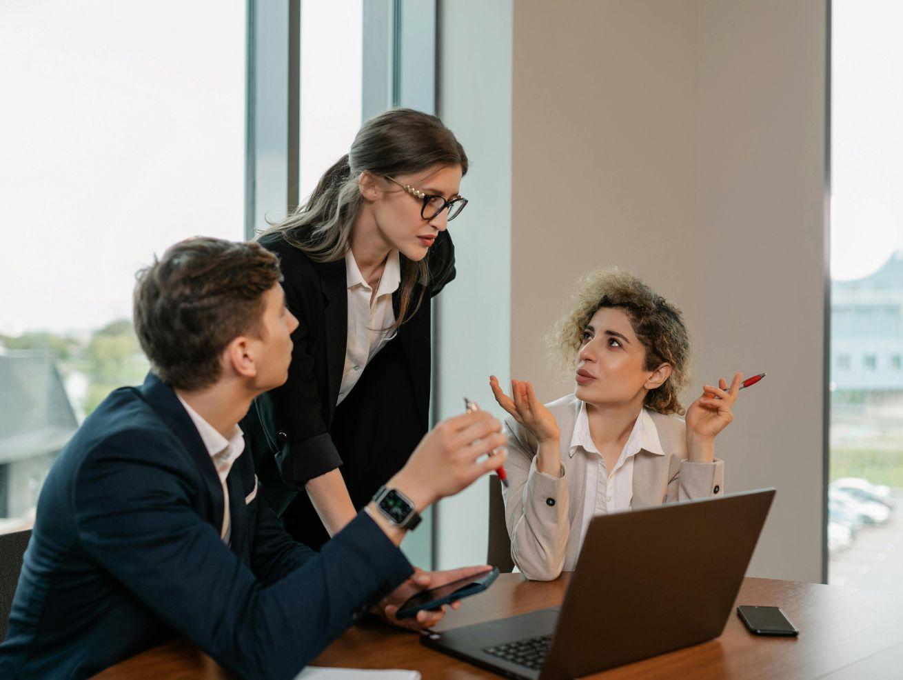 Three young lawyers looking at a laptop and discussing legal issues around a desk