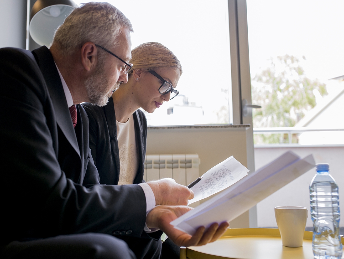 Male and female lawyers, both wearing glasses and looking at documents, working on a high-stakes litigation case.