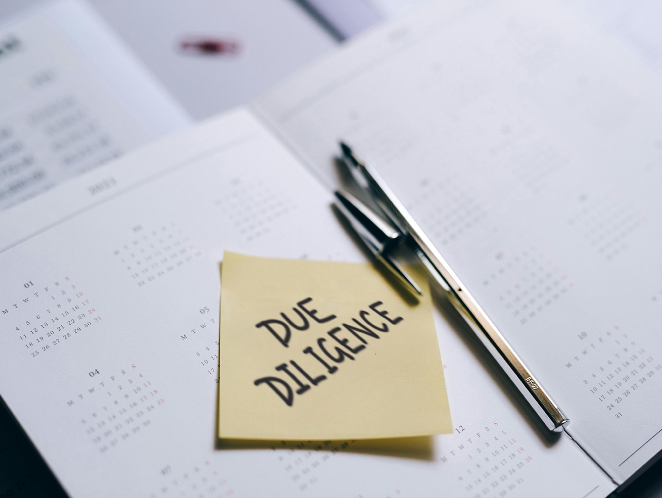 A pen laying on a sticky note that reads Due Diligence, atop a stack of legal papers